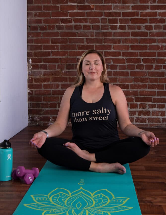 woman in tank on yoga mat doing lotus pose