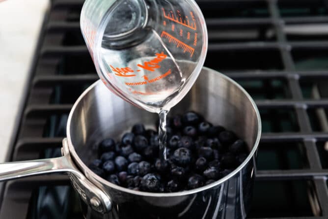 Process shot showing water being pourd into a saucepan full of blueberries