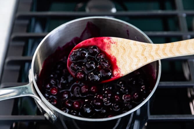 Blueberry filling in saucepan with wooden spoon showing it