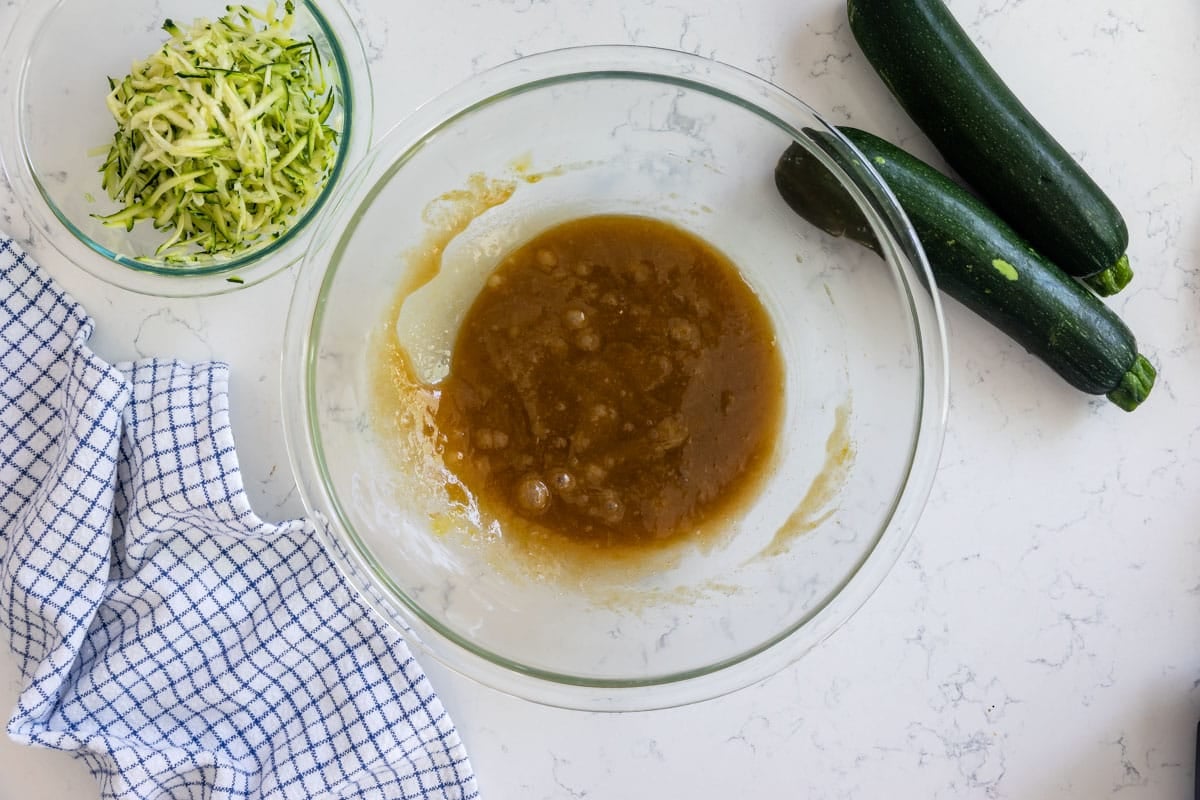 batter in glass bowl with bowl of zucchini shreds and zucchini next to.