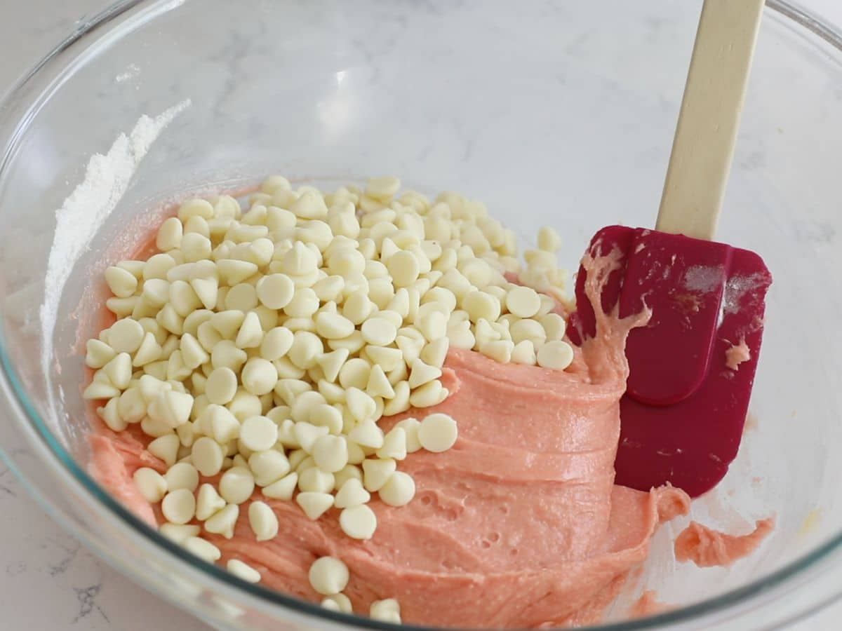 glass bowl with pink cookie batter and white chocolate chips and spatula.