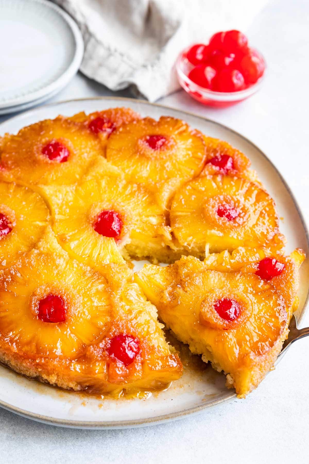 Overhead shot of pineapple upside down cake on a white rustic plate with one slice being pulled from cake