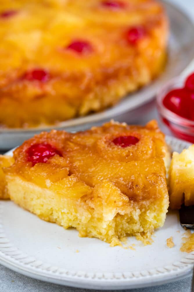 One slice of pineapple upside down cake with a bite missing on a plate with fork