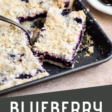 Blueberry slab pie in sheet pan with corner piece being scooped out with a serving spoon and recipe title on bottom of photo