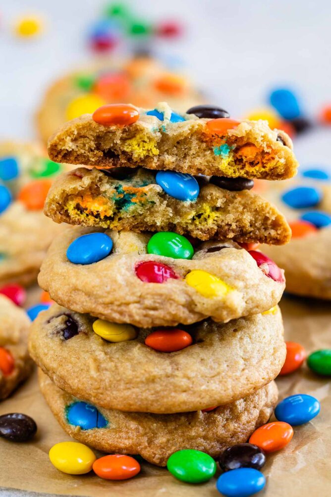 Stack of chocolate chip M&M cookies on parchment paper with top cookie cut in half to show M&Ms on the inside