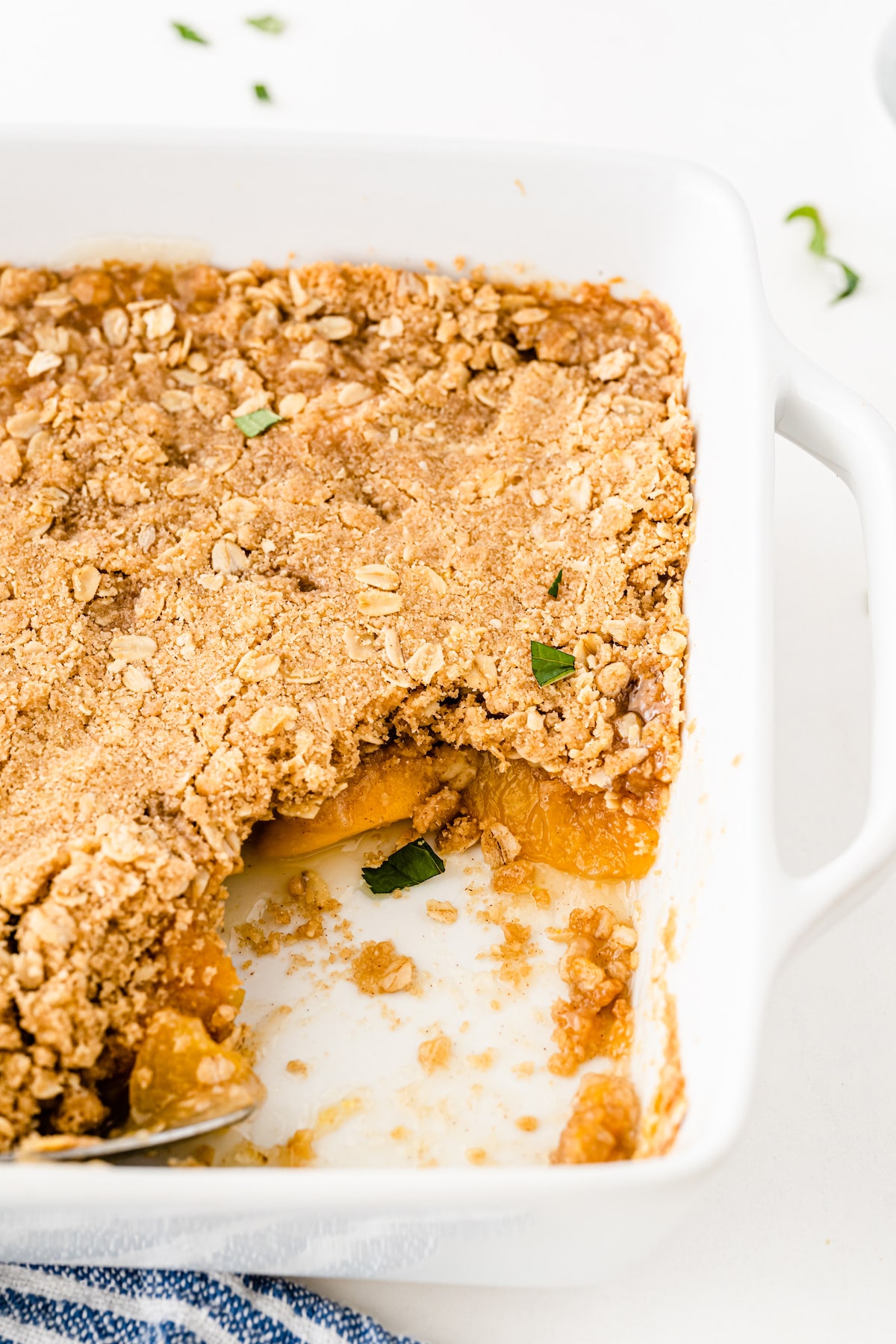 Peach crisp in a white baking dish with corner piece missing