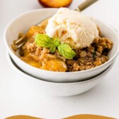 Bowl of peach crisp topped with vanilla ice cream and recipe title on bottom of photo