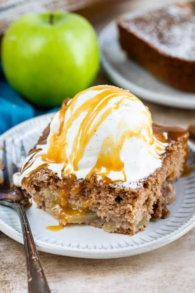 Slice of apple pie cake topped with vanilla ice cream and caramel sauce