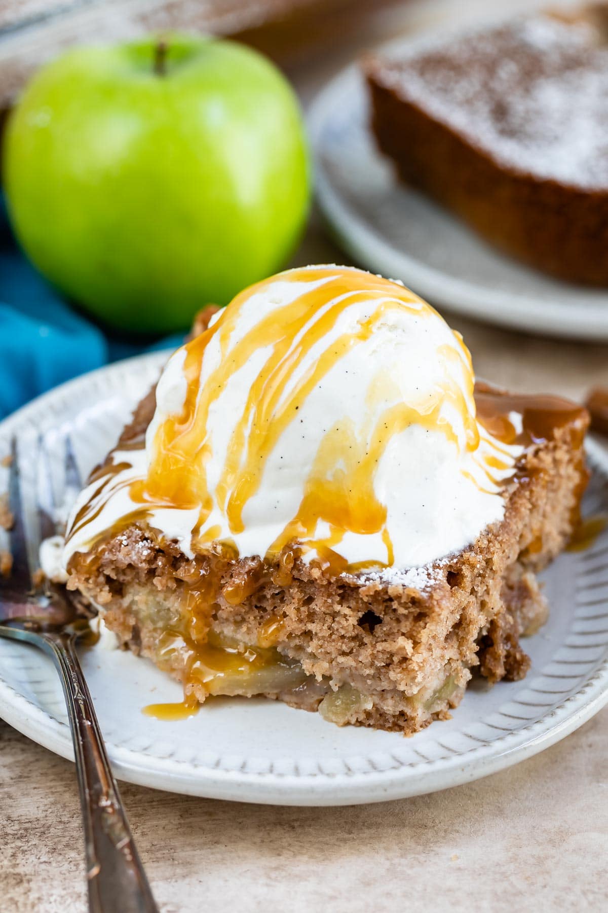 Slice of apple pie cake topped with vanilla ice cream and caramel sauce