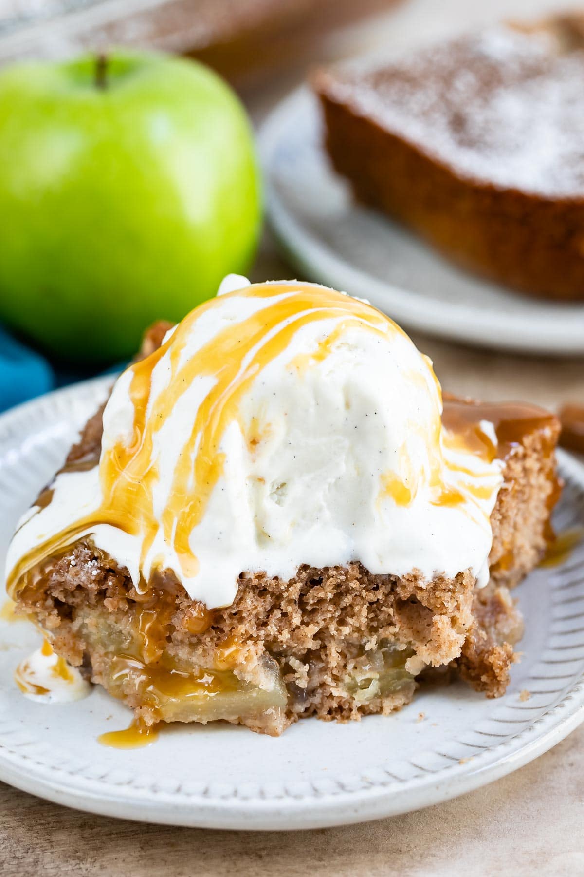 Slice of apple pie cake topped with vanilla ice cream and caramel sauce with one bite missing