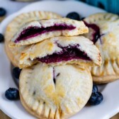 Blueberry hand pies on a plate with one split in half to show blueberry filling