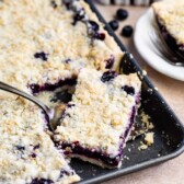 Blueberry slab pie in sheet pan with corner piece being scooped out with a serving spoon