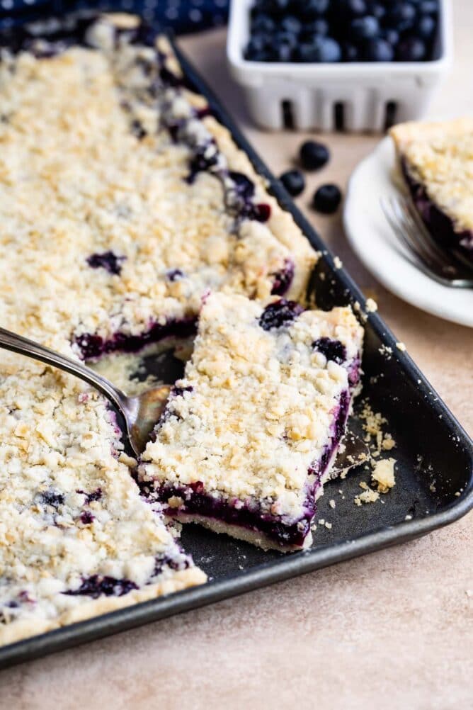 Blueberry slab pie in sheet pan with corner piece being scooped out with a serving spoon