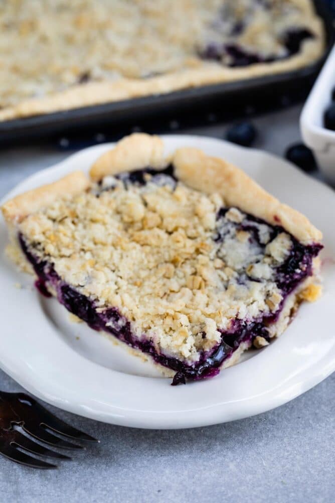 Corner piece of blueberry slab pie on a white dessert plate