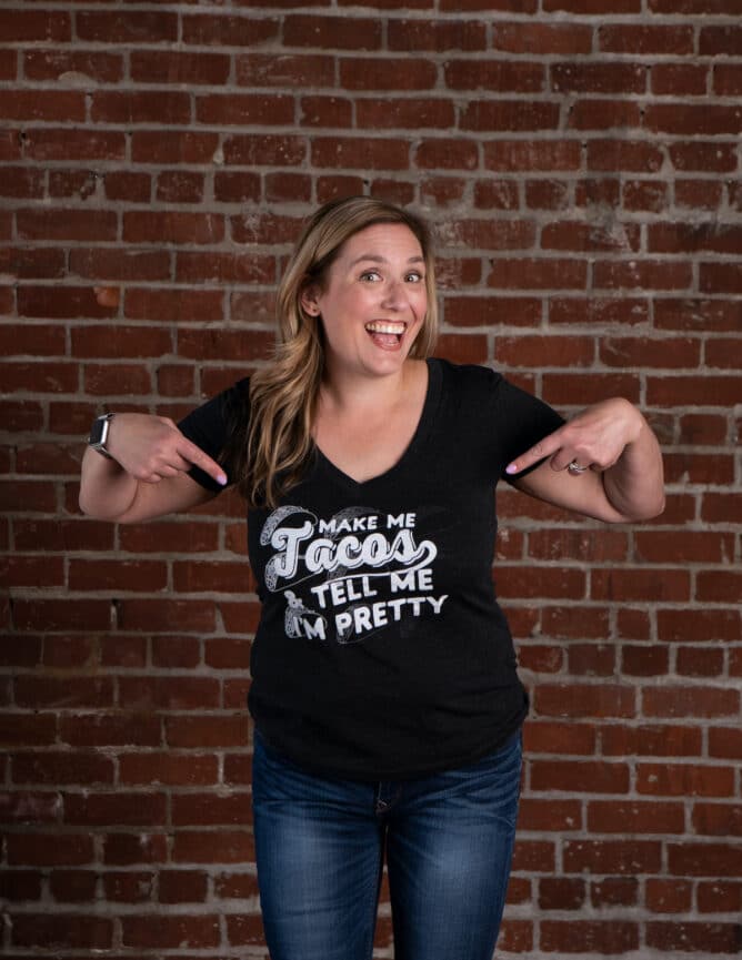 woman pointing at shirt in front of brick wall