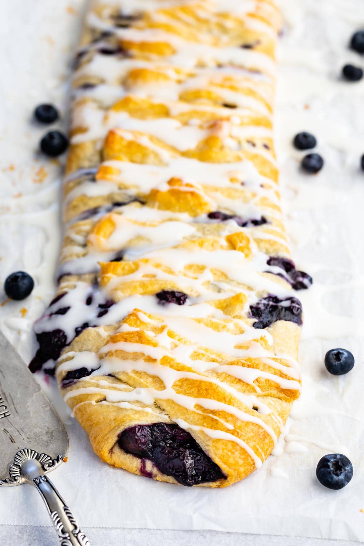 Blueberry danish with icing on top and blueberries spread around it