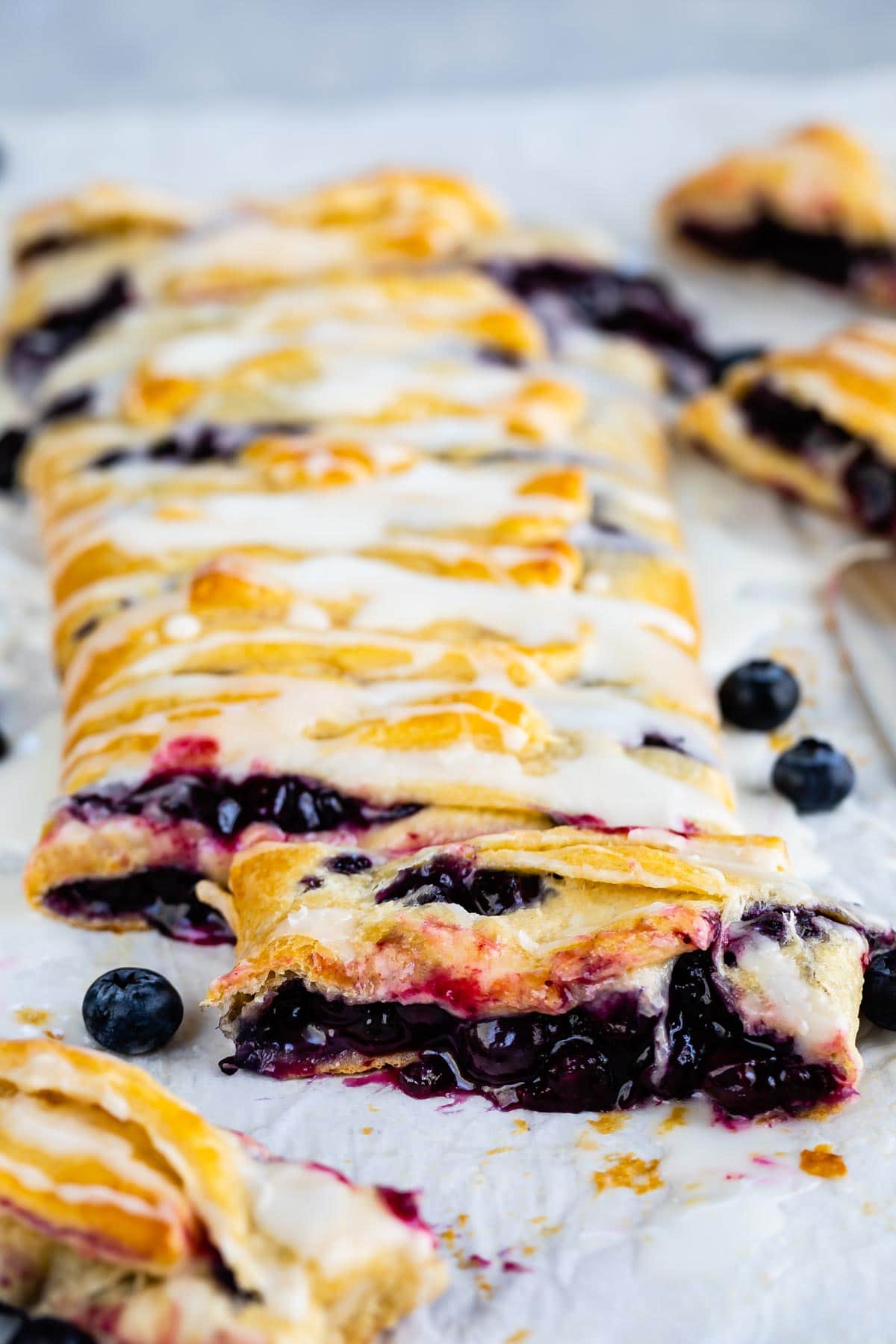 Blueberry danish with icing on top with one piece sliced on the end
