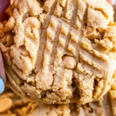 Hand holding one XL bakery style peanut butter cookie with recipe title on top of image