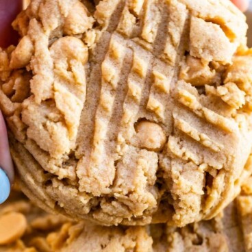 Hand holding one XL bakery style peanut butter cookie with recipe title on top of image