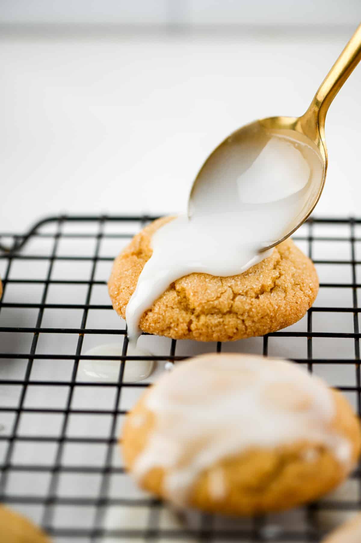 spoon drizzling icing over the top of cookie on rack.