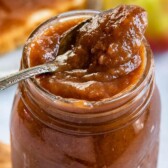 Apple butter in a mason jar with a spoon coming out and recipe title on top of image