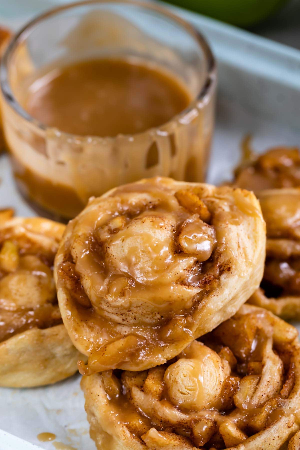 Easy caramel apple cinnamon rolls stacked on eachother with caramel sauce in the background