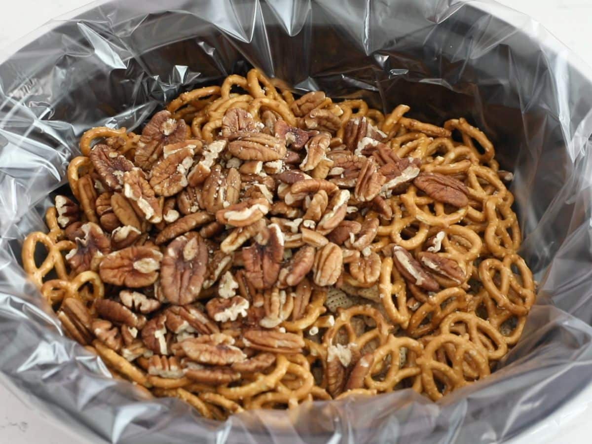 pecans, pretzels, and Chex mix in black slow cooker with liner