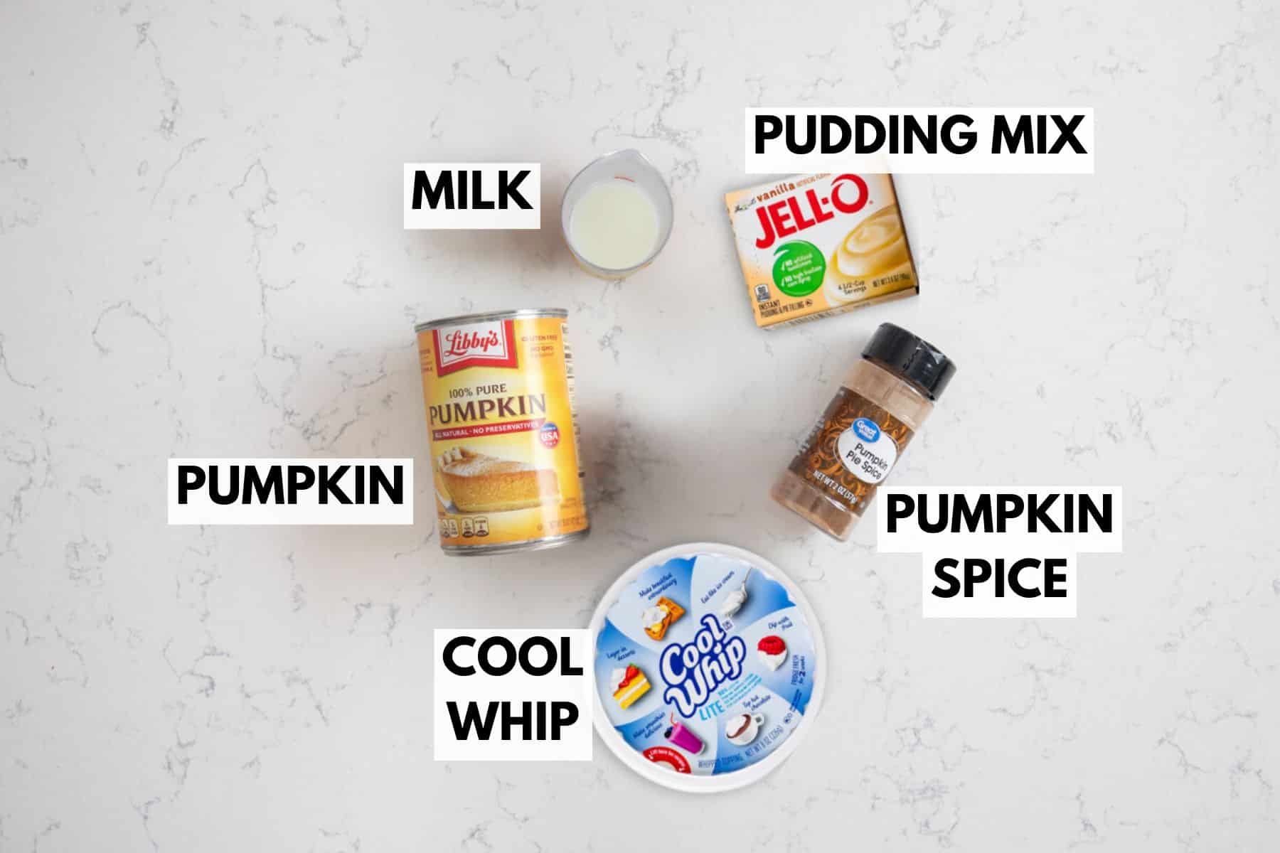 Canned pumpkin, Cool Whip, pumpkin spice, milk in a small cup, and vanilla pudding mix are arranged on a white surface. Each item is labeled for making delicious pumpkin fluff.