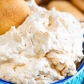 A bowl filled with creamy pumpkin fluff dip topped with a vanilla wafer cookie, with more cookies blurred in the background.