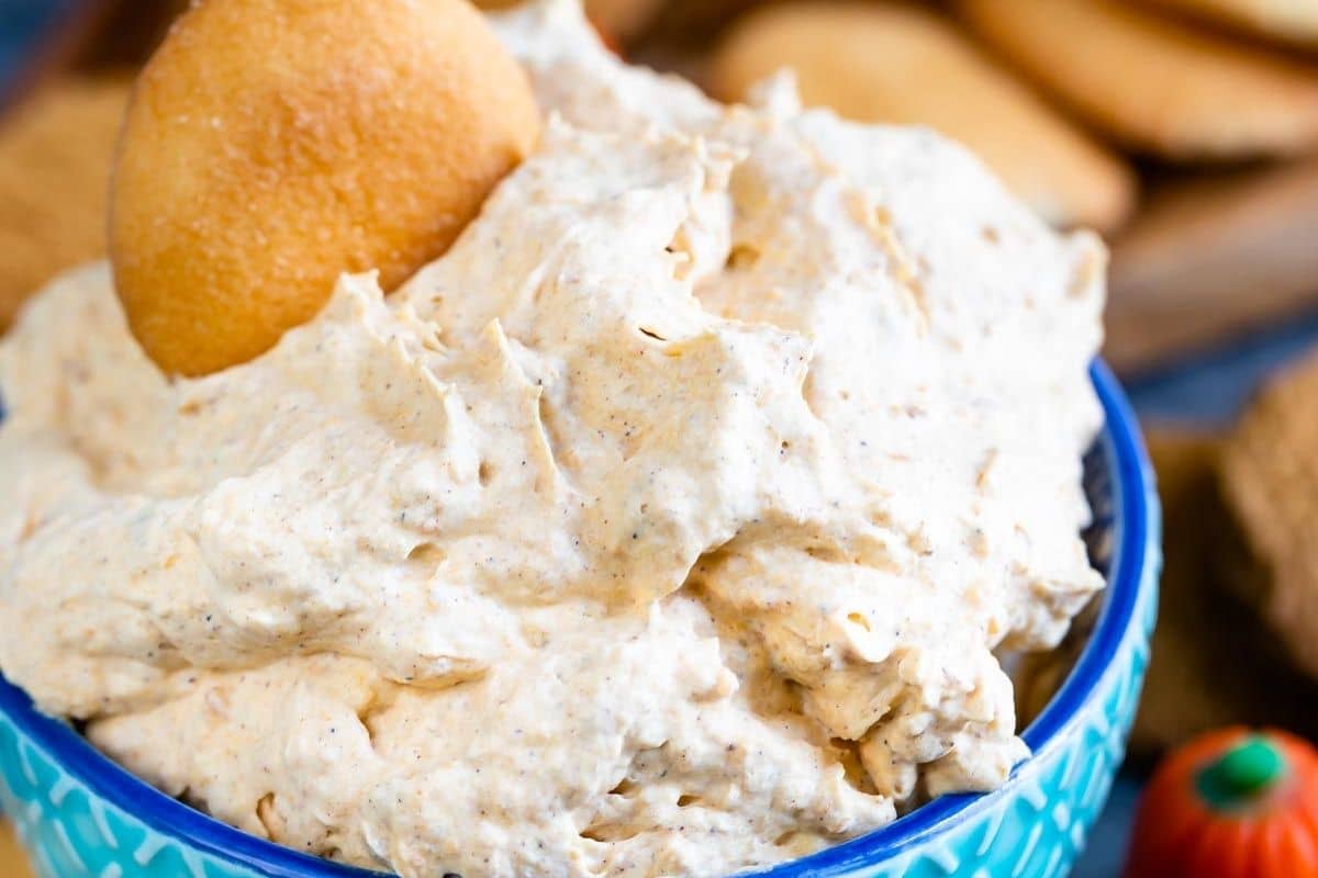 A bowl filled with creamy pumpkin fluff dip topped with a vanilla wafer cookie, with more cookies blurred in the background.