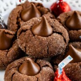 Plate full of chocolate peanut butter blossoms with Hershey kisses sprinkled on plate with recipe title on top of image