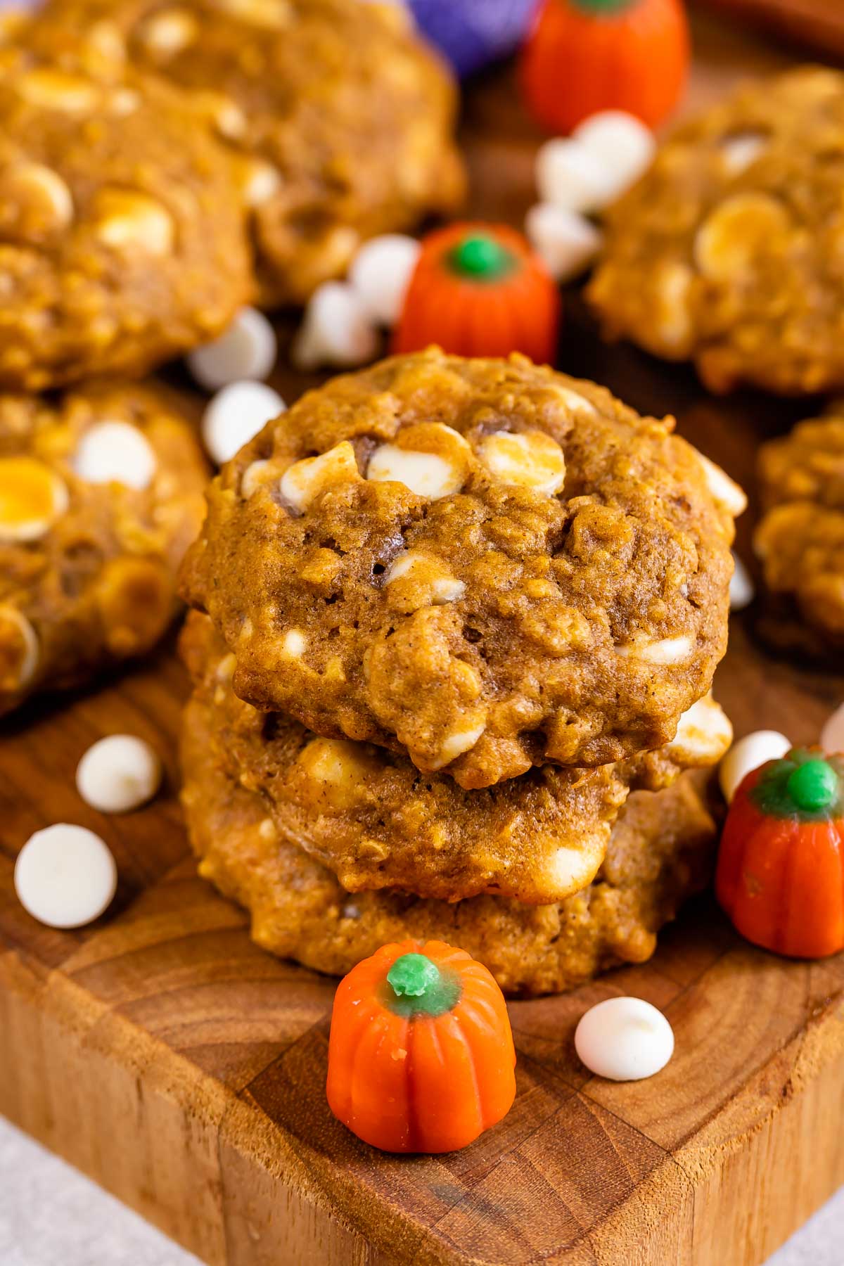 Pumpkin oatmeal cookies on a cutting board with pumpkin candies and white chocolate chips