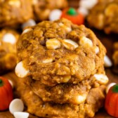 Pumpkin oatmeal cookies on a cutting board with pumpkin candies and white chocolate chips