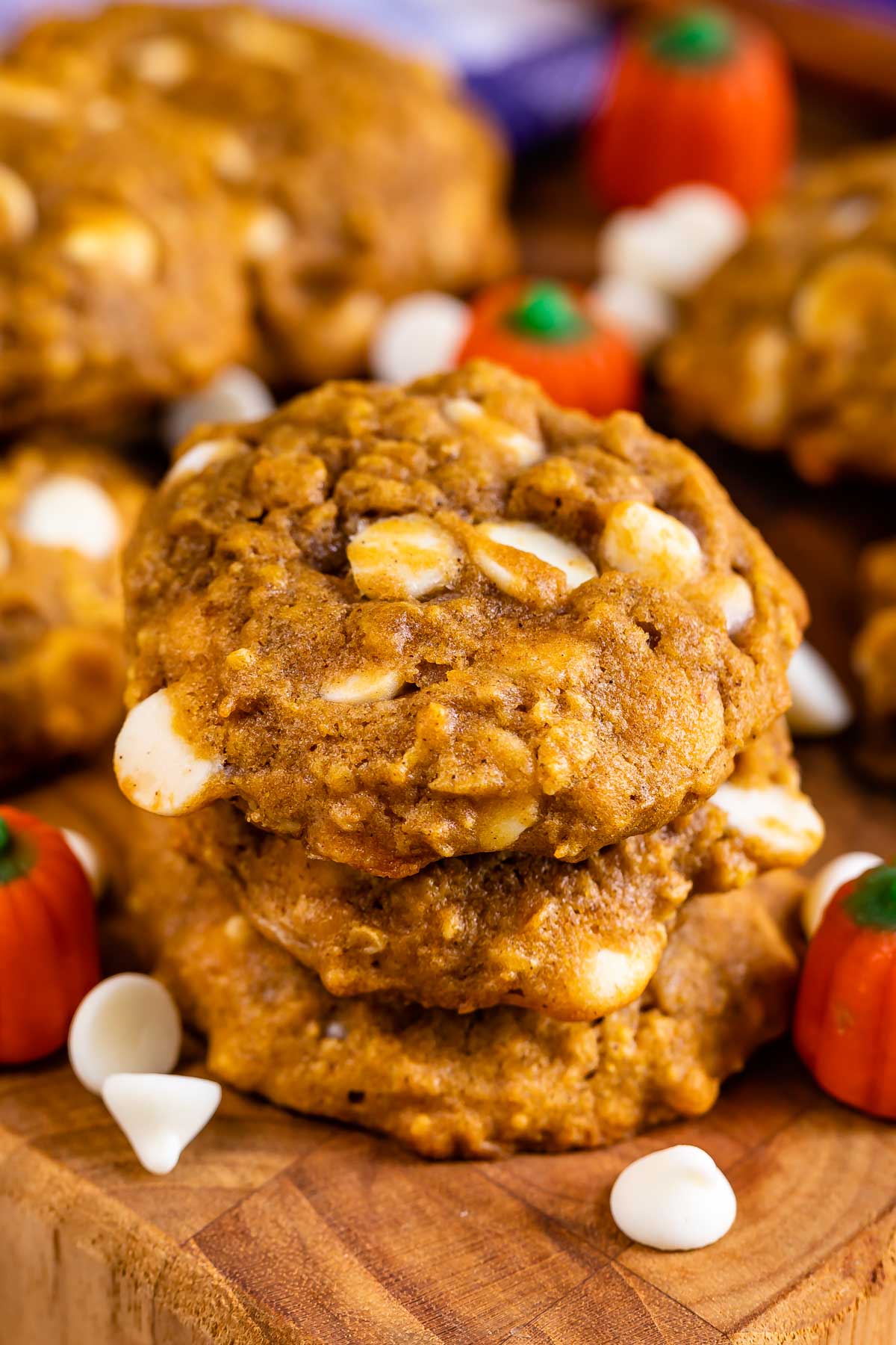 Pumpkin oatmeal cookies on a cutting board with pumpkin candies and white chocolate chips