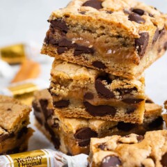 Stack of caramel chocolate chip cookie bars with candys around them