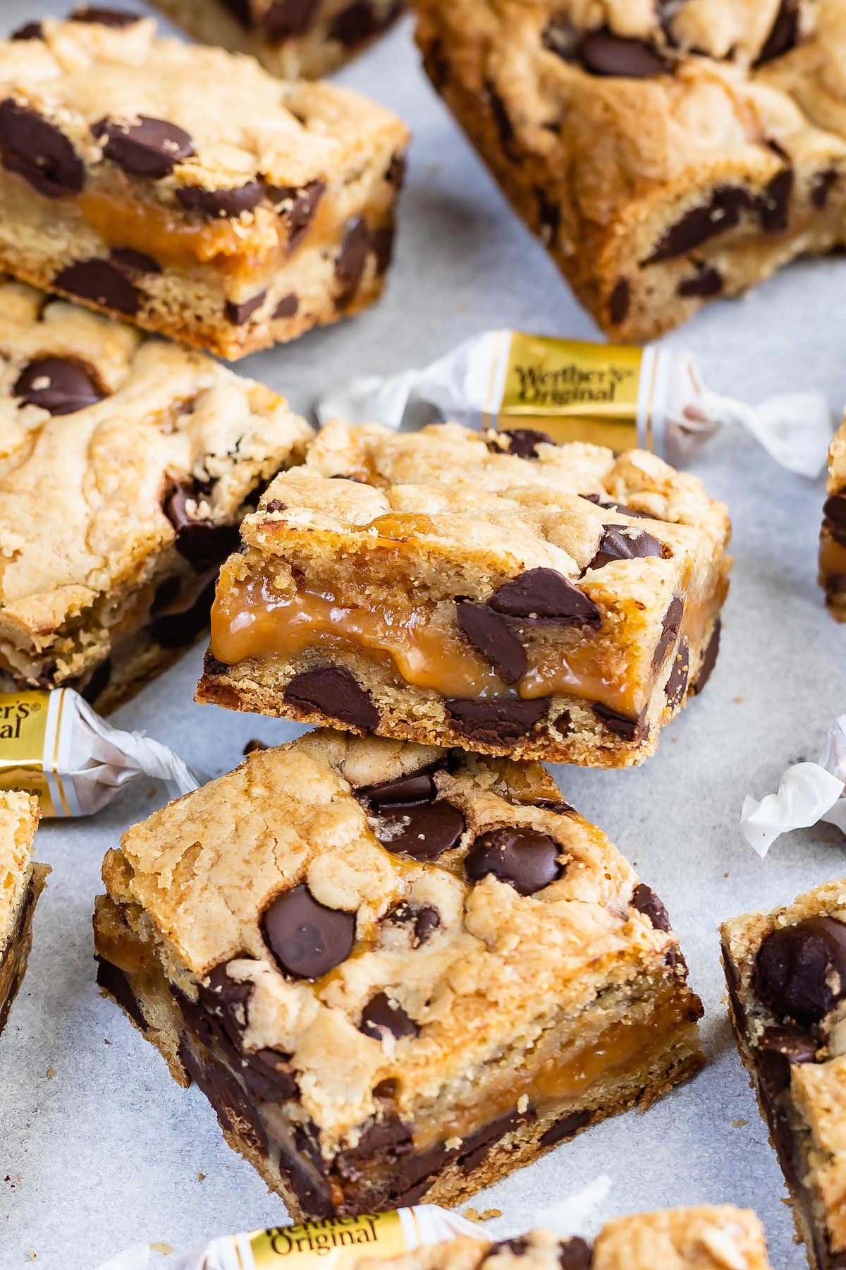 Close up shot of two caramel chocolate chip cookie bar squares with more cookie bars and candy around them