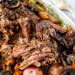 white serving platter with meat, potatoes and carrots around the edge