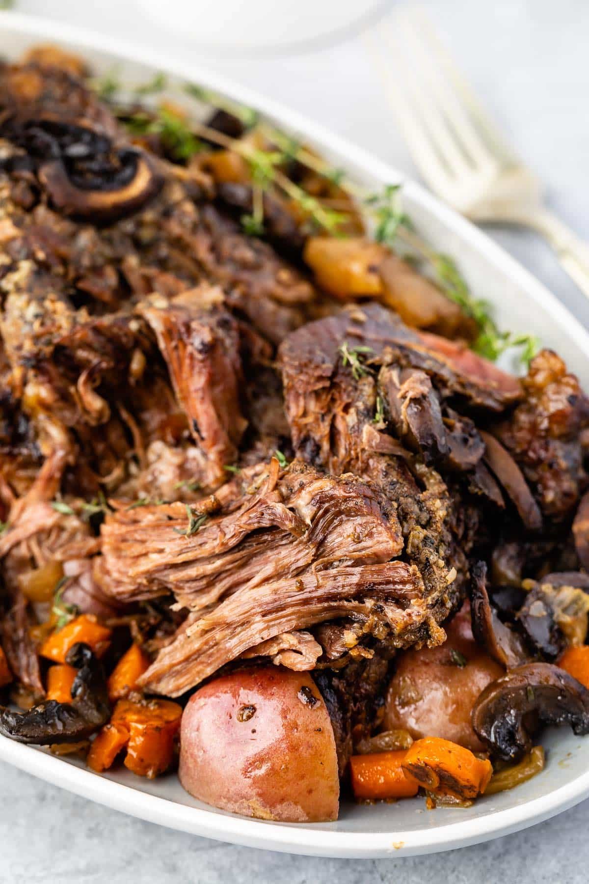 white serving platter with meat, potatoes and carrots around the edge