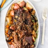 white serving platter with meat, potatoes and carrots around the edge with pitcher of gravy and carrots above