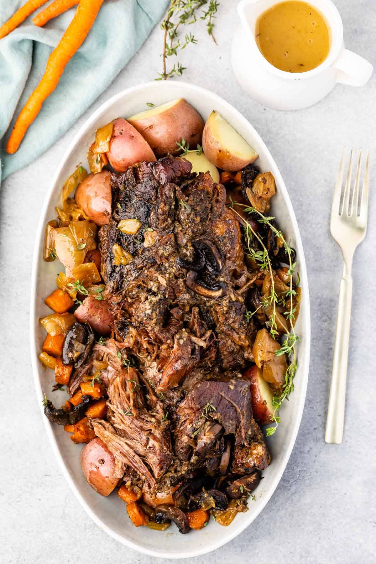 white serving platter with meat, potatoes and carrots around the edge with pitcher of gravy and carrots above