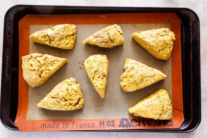 Overhead shot of pumpkin scones on a baking sheet with silicon mat