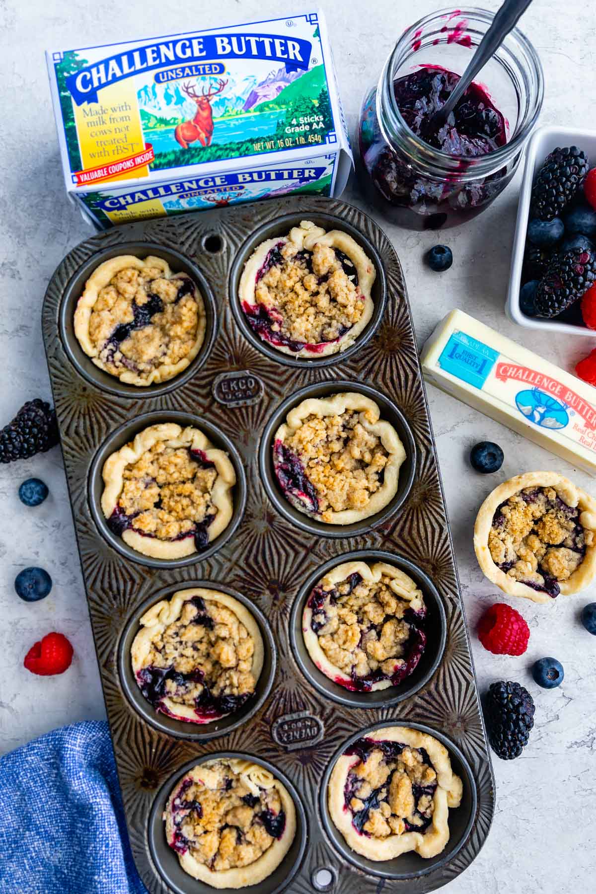 Overhead shot of mini berry pies in muffin tin with ingredients all around it