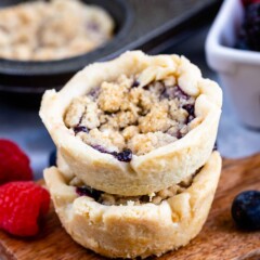 Two mini berry pies stacked on top of eachother surrounded by fruit