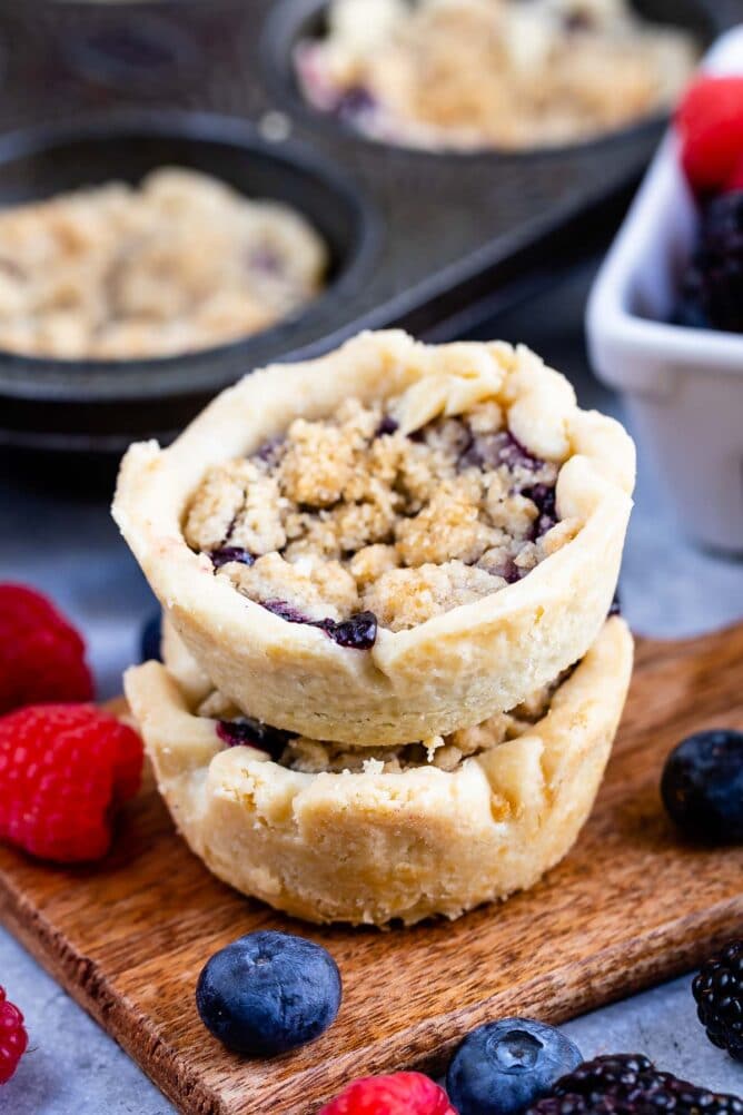 Two mini berry pies stacked on top of eachother surrounded by fruit