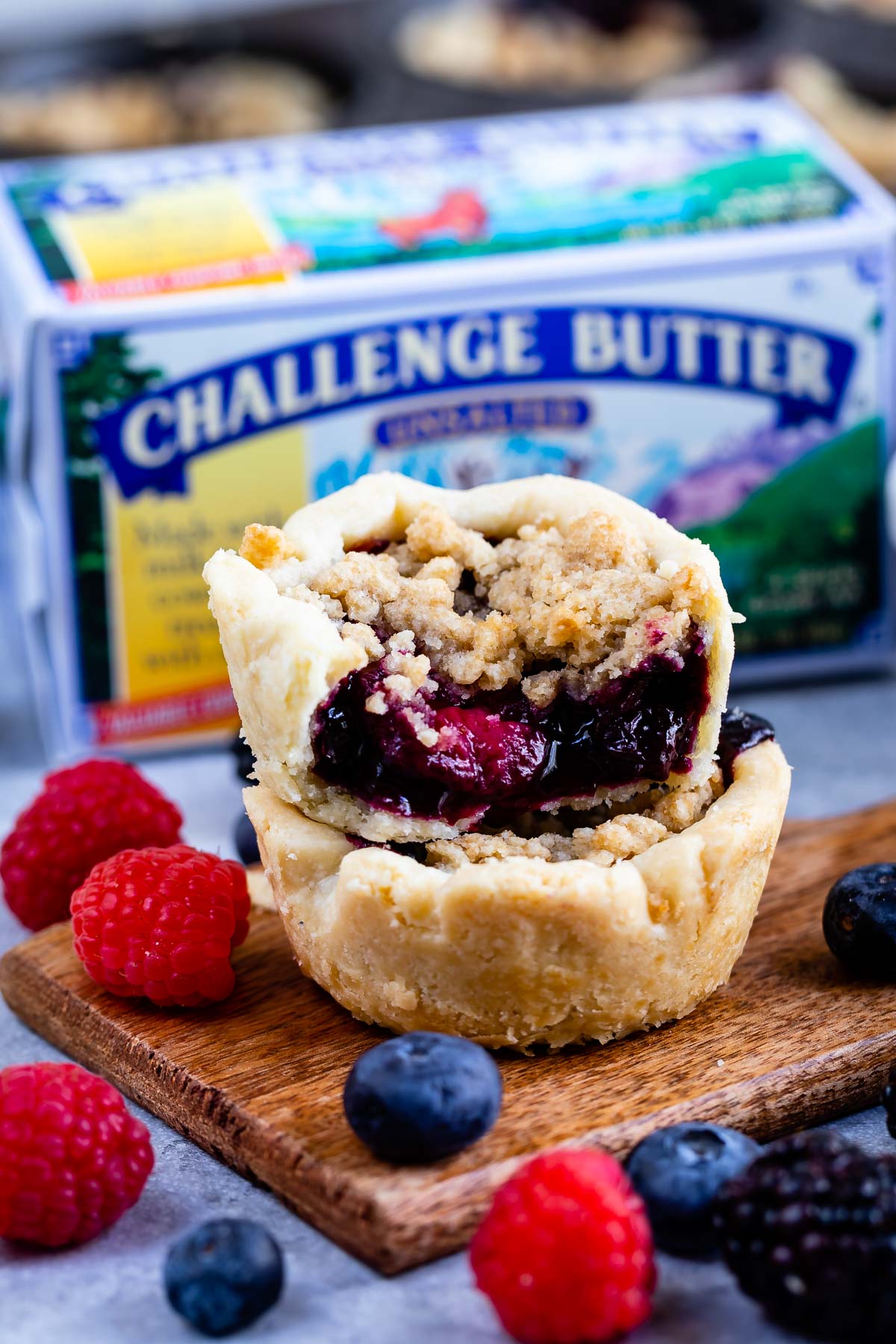 Two mini berry pies stacked on top of eachother with butter and fruit in the background