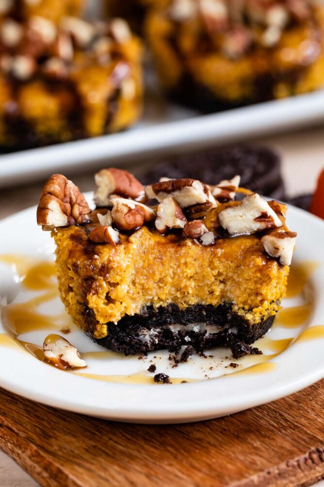 One mini turtle pumpkin cheesecake missing one bite with Oreo crust drizzled in caramel sauce