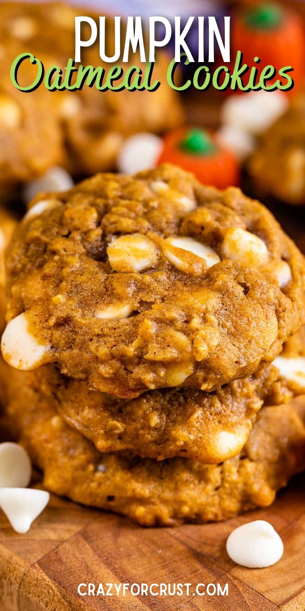 Pumpkin oatmeal cookies on a cutting board with pumpkin candies and white chocolate chips with recipe title on top of image