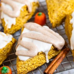 Pumpkin scones with icing on top surrounded by cinnamon sticks and pumpkin candies
