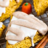 Pumpkin scones with icing on top surrounded by cinnamon sticks and pumpkin candies and recipe title on top of photo