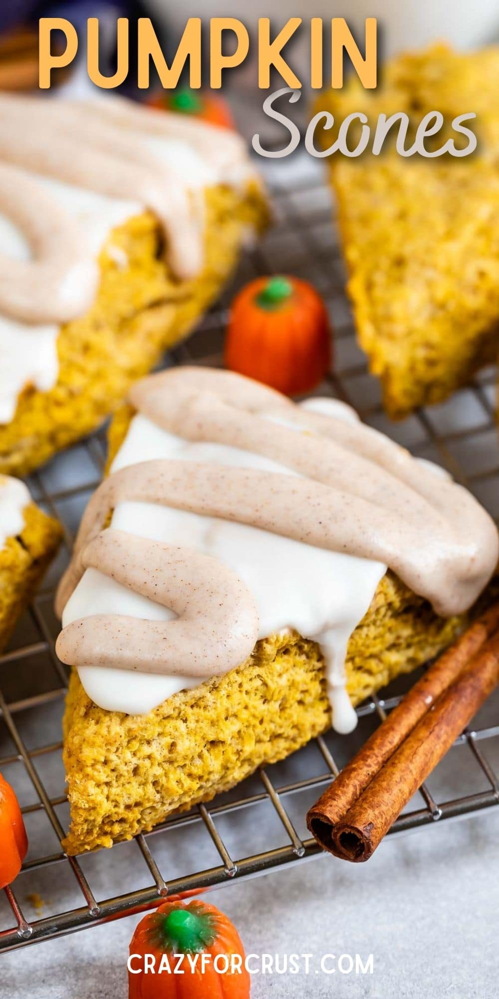 Pumpkin scones with icing on top surrounded by cinnamon sticks and pumpkin candies and recipe title on top of photo